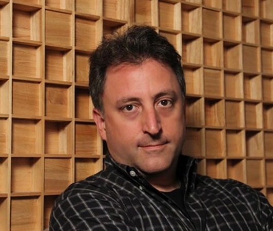 male voiceover engineer Bryant Falk, wearing black plain button down shirt standing in front of wood wall