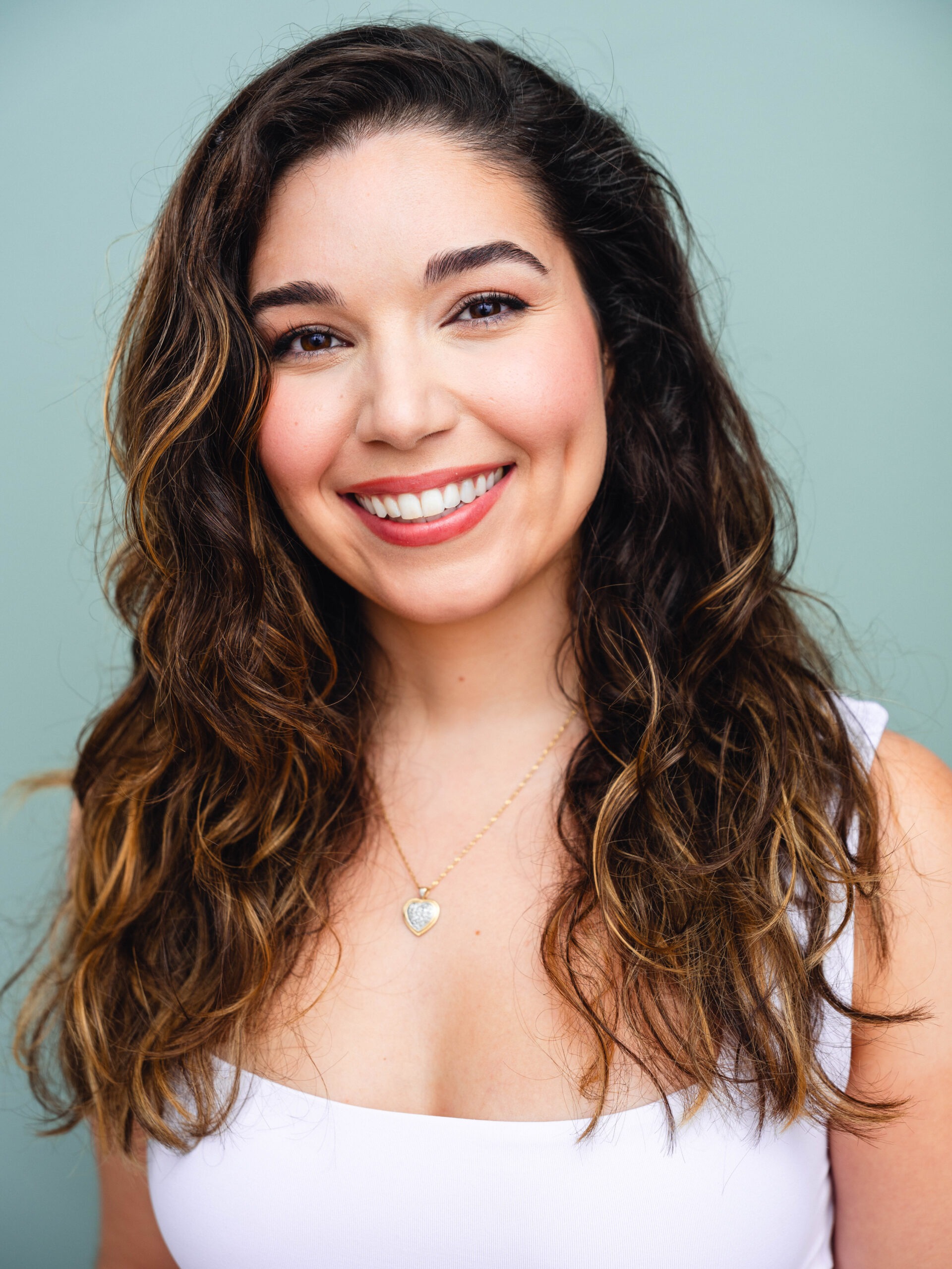 headshot of female voiceover coach Emma Romasco wearing a white shirt and standing in front of a blue background